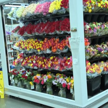 Costco Wholesale - A variety of flower bouquets in vases and plastic wraps are arranged on shelves in a store aisle, with a caution sign on the floor. - Gas Stations Near Me - Albuquerque, New Mexico
