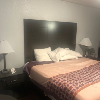 Budget Inn - Been here 4 days and I don't wanna leave! King size extremely soft with crisp clean sheets everyday - A hotel room features a bed with pillows, a dark headboard, and two bedside lamps on dark nightstands. - Hotels Near Me - Saint Augustine, Florida