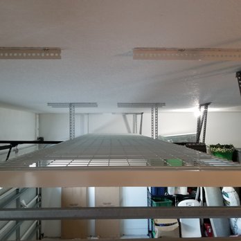 Garage Evolution - Side angle photo showing two 4x8 racks installed over the garage door.  These two racks will store sixteen of the 16" tall totes. - Cabinetry Near Me - Sarasota, Florida