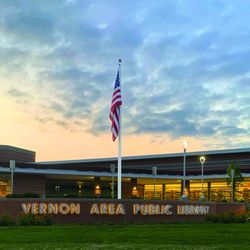 Vernon Area Public Library District - The US flag flies over the library entryway at dusk.