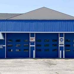 All Pro Servicenter - Wide exterior view showing the full blue building front, parking lot, and service bays of the Ankeny location on E 1st St.