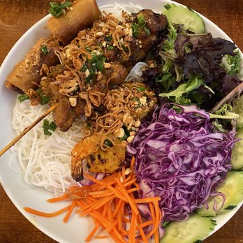 Bamboo by Kulantro - #2 with Grilled Chicken - A plate contains grilled meats on skewers, topped with fried shallots and chopped green onions, served alongside rice noodles, shredded carrots, purple cabbage, and sliced cucumbers. The presentation includes a variety of fresh vegetables and cooked meats, typical of Vietnamese cuisine. - Vietnamese Near Me - Albuquerque, New Mexico