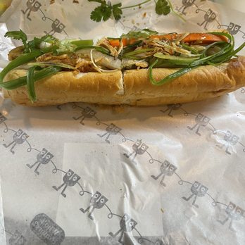 Tealux Cafe - Grilled Pork / Banh Mi Thit Heo Nuong - A sandwich with grilled pork, green onions, cilantro, and vegetables in a baguette, served on branded paper. - Bubble Tea Near Me - Ballwin, Missouri