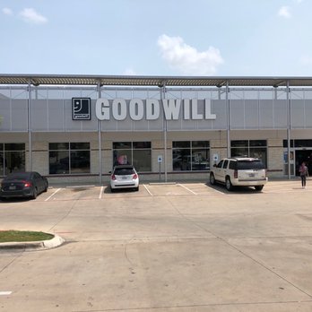 Goodwill Central Texas - Clock Tower - Store front - A large Goodwill store with a prominent sign on the facade is visible in the image. The building has a modern design with glass windows and a metal awning. The parking lot in front contains a few cars and a person walking toward the entrance. The sky is partly cloudy, and the overall scene depicts a typical retail storefront exterior. - Used, Vintage & Consignment Near Me - Austin, Texas