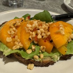 Open-faced tomato sandwich with smashed avocado, feta, and roasted corn salad.