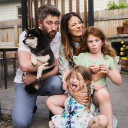 Megan Norman Photography - Playful family making silly faces with their dog on a backyard patio during an in-home family photography session.