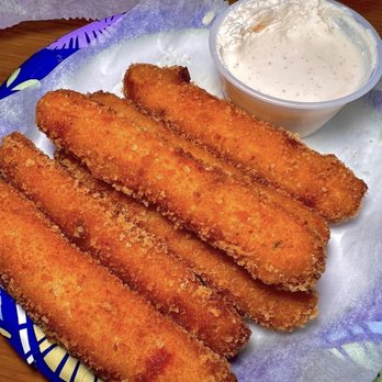 Freskos - Hamden - Feta Cheese Sticks - Four breaded and fried fish fillets are arranged on a plate lined with paper, accompanied by a small container of tartar sauce. The fillets are golden brown and crispy, typical of fried seafood dishes. The setting suggests a casual dining environment, likely at a Greek eatery that offers traditional dishes such as fish and seafood. The image emphasizes the texture of the breading and the creamy tartar sauce. - Greek Near Me - Hamden, Connecticut