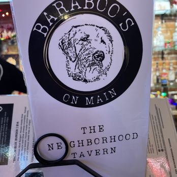 Baraboo's on Main - a sign for the neighborhood tavern - A menu featuring a dog illustration and the text "The Neighborhood Tavern" is placed on a table, with a black ring holder and some papers underneath. - Pubs Near Me - Dubuque, Iowa