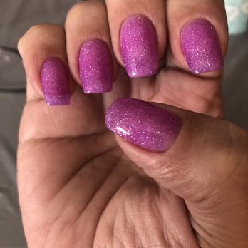 Charming Spa - Nails - The image shows a close-up of a hand with five fingernails painted in purple glitter nail polish. The nails are well-manicured, and the polish has a sparkly, textured appearance. The background is blurred, with a hint of a Minnie Mouse-themed item visible. The focus is on the nails, highlighting the detailed glitter finish. - Nail Salons Near Me - Brighton, Massachusetts