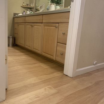 CD Kitchen & Bath Remodel - Flooring - A bathroom vanity with wooden cabinets and drawers, topped with a mirror and decorative items, is visible in the image. - General Contractors Near Me