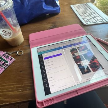 Satellite Coffee - A tablet in a pink case shows a photo editing app open on a wooden table, with a pink stylus nearby, alongside a drink, a keychain, and a keyboard. - Coffee & Tea Near Me - Albuquerque, New Mexico