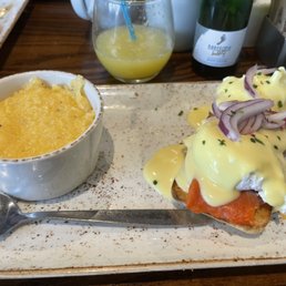 Smoked Salmon & Roasted Vegetable Frittata - Eggs Benedict topped with smoked salmon, served with cheesy grits and a glass of orange juice at a restaurant table.