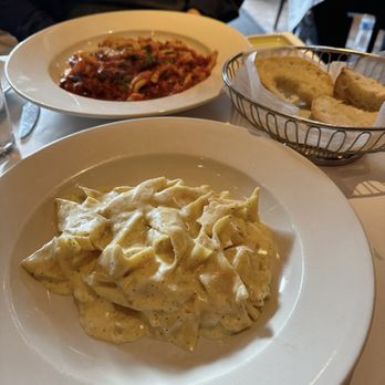 Casarecce - Lamb Ragu (back) and Pappardelle Alfredo (front). Loved the Pappardelle Alfredo! - A plate of fettuccine Alfredo with a creamy white sauce and black pepper is on a table at an Italian restaurant, with bread in a basket nearby. - Italian Near Me - Boston, Massachusetts