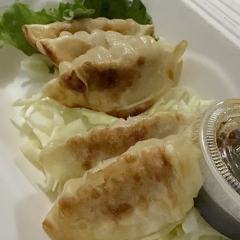 Sushi Pure - Gyoza - Three gyoza dumplings are arranged on shredded cabbage, with a small container of dipping sauce nearby, on a white takeout plate. - Sushi Bars Near Me - Eugene, Oregon