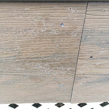 Felcor Construction Corp. - Fascia board delivered by XPO Logistics/Lowe's damaged was installed by Felcor anyway! - A photograph of a wooden surface composed of multiple planks, with visible screws securing the planks. The wood has a weathered appearance with visible grain, scratches, and some white paint or residue. The surface appears to be part of an outdoor structure or furniture, with a patterned surface visible at the bottom edge of the image. - General Contractors Near Me