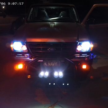Auto Depot - NEW LIGHTS INSTALLED BY AUTO DEPOT. - The image shows a Ford vehicle parked outdoors at night, with its headlights and fog lights turned on, casting bright light. Additional off-road lights are mounted on the front bumper, also illuminated. The vehicle's front door on the passenger side is open, and a license plate with the word 'NAVY' is visible. The background includes another vehicle and a dark environment, with the timestamp indicating the photo was taken on June 6, 2024, at 9:07 AM. - Auto Detailing Near Me - Albuquerque, New Mexico