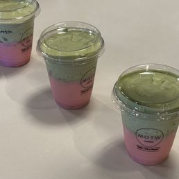 Strawberry Matcha waiting for their owners - Three layered beverages in clear plastic cups with lids, featuring pink, green, and clear layers, placed on a white table.