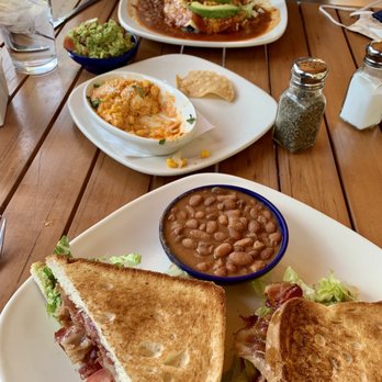 Cafe Abiquiu - BLT with avocado and a side of pintos. The elote dip was yummy, too! - The image shows a wooden table with Mexican food items such as sandwiches, beans, guacamole, and side dishes, along with salt, pepper, and sugar shakers. - Mexican Near Me - Abiquiu, New Mexico