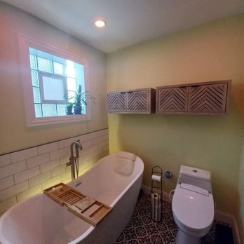 AR Remodeling Group - bathroom 3 - A bathroom features a freestanding bathtub with a wooden bath tray, a modern toilet, a window with potted plants, and wall-mounted cabinets. - General Contractors Near Me - Chicago , Illinois