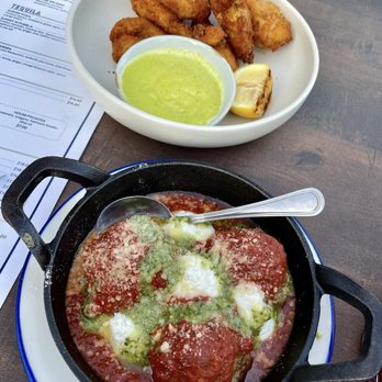 The Clifton - A table features two dishes: one with fried food and green dipping sauce, and another with meatballs topped with cheese and green sauce. - Pizza Near Me - Plainfield, Illinois