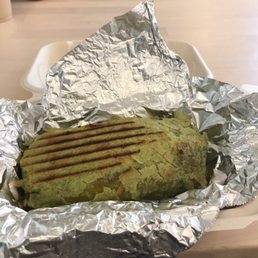 Breakfast Burrito - A green-colored grilled sandwich with grill marks, wrapped in aluminum foil, placed on a table in a casual setting.