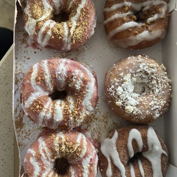 Duck Donuts - Six donuts with different toppings and glazes are arranged in a white box, featuring drizzles, powdered sugar, and crumb toppings. - Donuts Near Me - Paramus, New Jersey