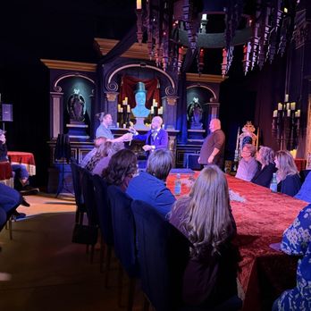Mystique The Magic Experience - Audience members sit at a long table watching a magic show on stage in a theater with ornate decor and candles. - Magicians Near Me - Mesa, Arizona