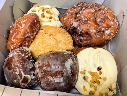 Photo of Kamehameha Bakery - Honolulu, HI, United States. Assorted pastries (apple turnover, apple fritter, cinnamon pastry with cream cheese frosting, poi and orange donuts)