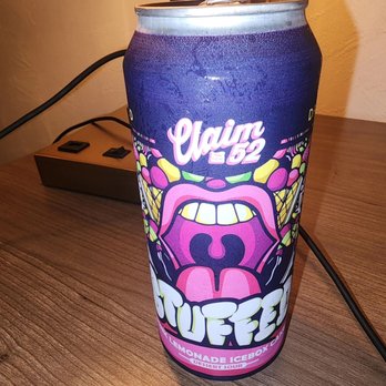 The Maverick Hotel - A tall, cylindrical soda can features a colorful, psychedelic design with a stylized mouth and tongue graphic, and the label 'Claim 52 Lemonade Icebox' indicating a dessert sour flavor. The can is positioned on a wooden surface with a power strip and cords visible in the background, suggesting an indoor setting. - Hotels Near Me - Eugene, Oregon
