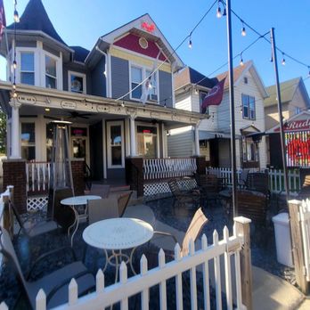 Rudy's - A Victorian-style building with a porch, outdoor tables, and string lights hanging overhead, situated in a neighborhood setting. - Tobacco Shops Near Me - Fort Wayne, Indiana