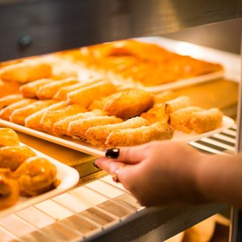 CAO Bakery & Cafe - A person placing a tray of croquettes in the display. - Bakeries Near Me - Miami, Florida CAO Bakery & Cafe - A person placing a tray of croquettes in the display. - Bakeries Near Me - Miami, Florida
