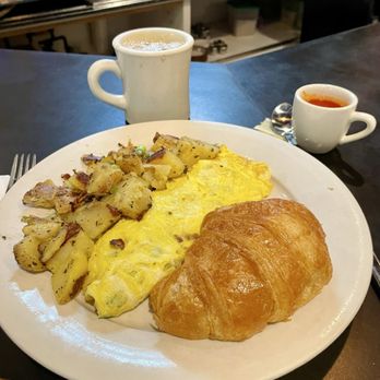 Bella's Cafe - Omelette with home fries and the best croissant in a long time. - A breakfast meal featuring an omelet, roasted potatoes, a croissant, and two cups of coffee or tea, served on a white plate at a cafe. - Breakfast & Brunch Near Me - New Haven, Connecticut