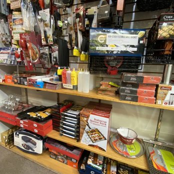 Kitchen Concepts - Store shelves hold grilling accessories, including skewers, sauce bottles, and cookware such as a barbecue skewer rack and a grill pan. - Kitchen & Bath Near Me - Mesa, Arizona