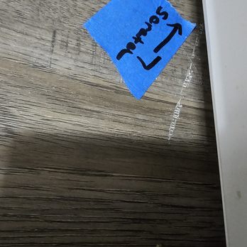 Express Flooring - A blue tape piece with handwritten text is affixed to a wooden surface near a white object. - Flooring Near Me - Rio Rancho, New Mexico