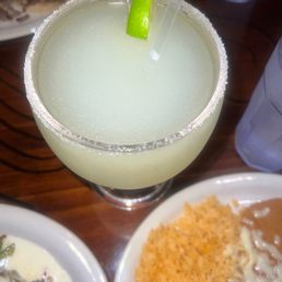 Lime margarita, beans and rice, mushroom supreme quesadilla - A lime margarita with a salted rim and a lime wedge, served in a glass with a straw, on a wooden table with food and drinks nearby.