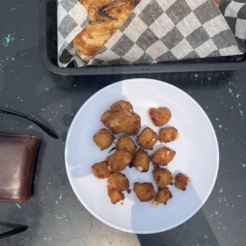 Bread and Butter Kitchen - Cheese curds - A white plate holds fried food pieces, placed on a dark table, with a loaf of bread wrapped in checkered paper in a black tray. - Breakfast & Brunch Near Me - Annapolis, Maryland