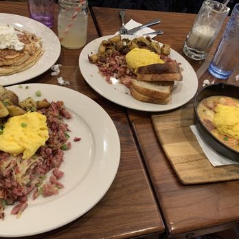 Bella's Cafe - Hash - A breakfast table features pancakes with whipped cream, scrambled eggs, roasted potatoes, toast, and a skillet with eggs and shrimp. - Breakfast & Brunch Near Me - New Haven, Connecticut