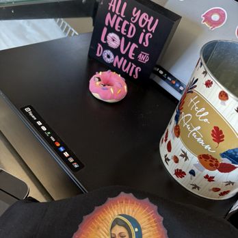 Mr Maple Donuts - love with doughnuts - A pink donut with sprinkles is placed on a black surface next to a sign that reads 'All you need is love and donuts.' A decorative container with autumn leaves and mushrooms is also visible. - Donuts Near Me - Phoenix, Arizona