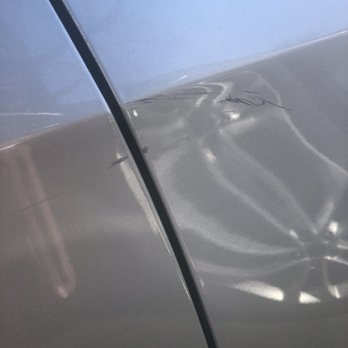 Xclusiv Auto Detail - The image depicts a silver car's side panel with a noticeable dent and multiple scratches around the area. The surface reflects light, highlighting the damage, and the photo appears to be taken at close range, focusing on the affected section of the vehicle. - Auto Detailing Near Me