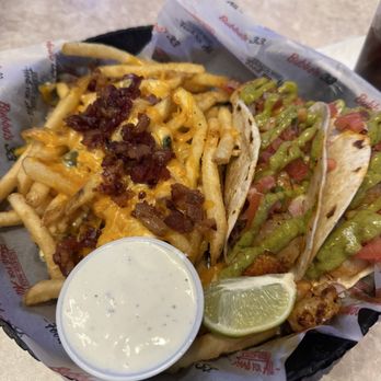 Bubba's 33 - Grilled shrimp tacos and loaded seasoned fries. - A basket contains two tacos with grilled chicken, diced tomatoes, and green sauce, accompanied by French fries topped with shredded cheese and bacon bits. A lime wedge and a small cup of creamy white sauce are also included. The basket is lined with branded paper from Bubba's 33, and the setting appears to be a casual dining restaurant. - Pizza Near Me - Evansville, Indiana