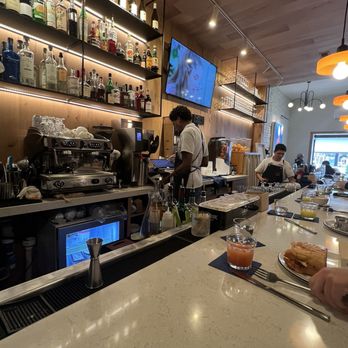 I Egg You - Bar - A bar interior with shelves of liquor bottles, bartenders working behind the counter, and a TV screen on the wall. - Breakfast & Brunch Near Me - Washington, DC, District of Columbia