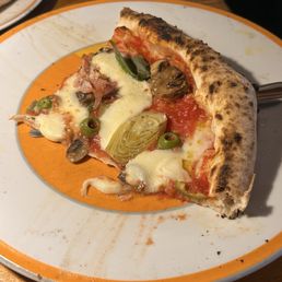 Quattro stagioni pizza - A pizza slice with cheese, green olives, artichoke, mushrooms, and tomato sauce on a white and orange plate.