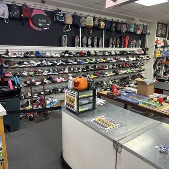 The Cave - Shoes behind the counter I wanted to take a look at. - A thrift store interior with multiple shelves filled with shoes, backpacks, and collectibles, and a counter with various items and a cardboard box. - Music & DVDs Near Me - Folsom, California