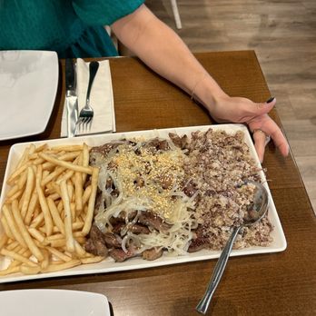 Boteco Do Manolo - A rectangular plate contains French fries, beef with onions, and a bread crumb topping, set on a wooden table at a restaurant. - Brazilian Near Me - Framingham, Massachusetts