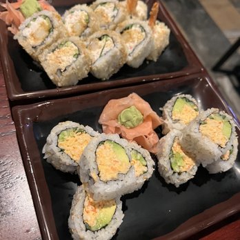 Senor Sushi - Sushi rolls - Two black rectangular plates contain assorted sushi rolls with ingredients such as avocado, tempura shrimp, and rice. The rolls are garnished with wasabi and pickled ginger. The setting appears to be a restaurant with a wooden table surface visible in the background. - Japanese Near Me - Phoenix, Arizona