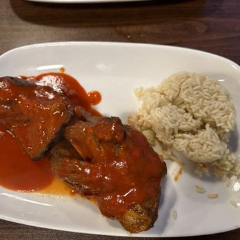 Efesus Cafe - Lamb Shank - A white plate holds a lamb shank covered in tomato sauce and a serving of rice, served at Efesus Cafe in Ashburn, VA. - Mediterranean Near Me - Ashburn, Virginia