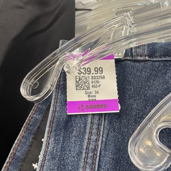Savers - $40... - The image shows a pair of denim jeans hanging on a clear plastic hanger. A price tag is attached to the hanger, displaying a price of $39.99, along with a QR code, product code, size 34, and indicating they are men's jeans. The jeans have visible stitching and are placed against a background that appears to be part of a retail store environment. - Thrift Stores Near Me - Santa Clara, California