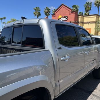 Dan's Window Tint - Tacoma - A silver pickup truck with tinted windows is parked in a parking lot near a Taco Bell restaurant, with palm trees and other vehicles visible. - Auto Glass Services Near Me - Phoenix, Arizona