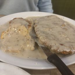 Chicken Fried Steak - A plate of country fried steak covered in gravy, accompanied by mashed potatoes with gravy, on a white dish.