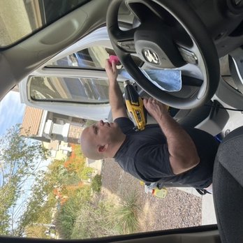 Wulf Window Tinting - A man is repairing or installing something on a vehicle's door using a yellow power drill, outside a house with trees and buildings in the background. - Car Window Tinting Near Me - Avondale, Arizona